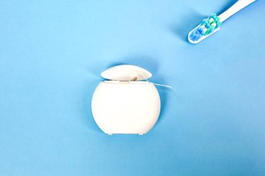 Mavi arka planda diş ipi ve diş fırçası kabı, diş bakımı ürünleri. Diş bakımı, sağlıklı yaşam tarzı, diş ipinden yararlanma, diş ipiyle ilgili önemli şeyler.