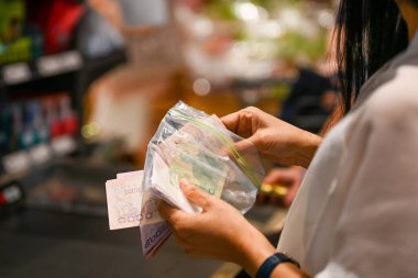 Asyalı bir kadın Tayland banknotunu, satın alma noktasını nakit olarak, hijyen depolama ve uygun kullanım için şeffaf plastik poşet içinde öder. şehir yaşam tarzı hijyen fonksiyonel kullanım kavramı