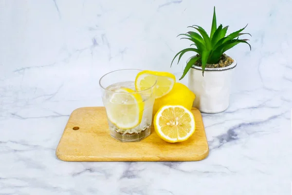 Lemon infused water, lemon cut in half on wooden plate and little tree pot on white marble background, infused water refresh your health, stay hydrated, benefits from infused water. stay healthy drink lemon infused water , stay hydrated