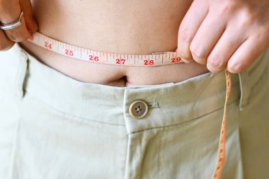 Slim young woman measuring her waist with a tape measure, success in loose fat, diet weight management. Slim slender figure.