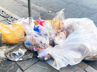 A little refuse bin overloaded with rubbish with a lot of litter around and mess and garbage everywhere on the street waiting to collect.