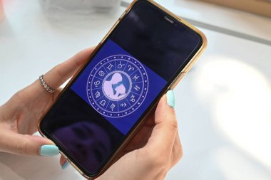 Hand holding smartphone checking Astrological zodiac horoscope Mobile application . Spiritual new age, wheel of fortune, fate karma and destiny