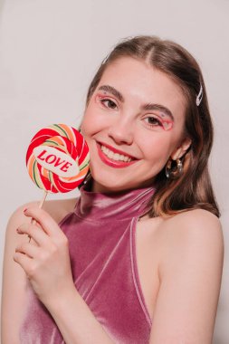 young beautiful girl with red candy in her hand on a gray background