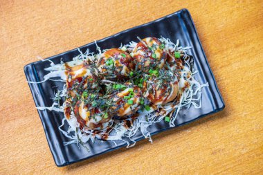 Ahtapot filetosu Takoyaki Garnitür ve yosun. Siyah bir tabakta doğranmış beyaz lahana ve soğan, Saimoden, ahşap bir masada daire içine alındı.