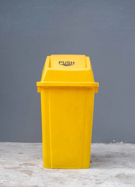 Yellow trash bin placed on the cement floor in a public place, trash bin, vertical photo, environmental concept