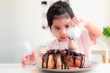 4-5 yaşlarında, şirin Asyalı bir kız kahve dükkanındaki beyaz bir masaya çikolatalı tost döker ve gülümser. Ballı Tost çocukların sevdiği tatlı bir tatlıdır.