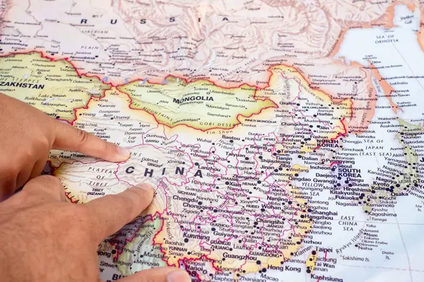 Tourist\'s hand pointing at world map of China. Located in Asia on world map, China is a country with a large area and a large population. top view