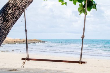 Sahildeki ağaçtan sarkan ahşap salıncak. Batan güneşin altında nehir kıyısında salıncak. Tatilde seyahat etme konsepti.