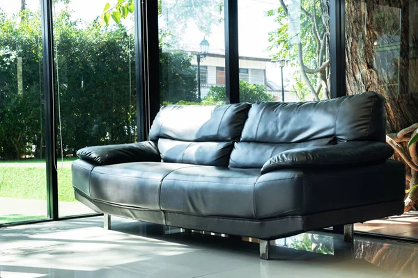 Cozy black leather sofa in composition with clear glass window in living room and sunlight with green garden outside, Cozy Interior concept ,minimal style