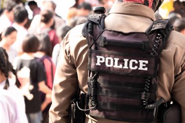 Erkek polis memurunun arkadan görünüşü. Sırtındaki kurşun geçirmez yelek polis kelimesini ortaya çıkarıyor. Tayland polis üniforması, barışın korunması ve korunması