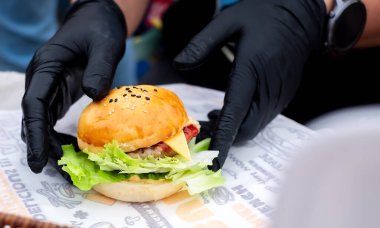 Hambuger mini, Professional  Hand chef holding fresh delicious and tasty handmade burger, garnished with salad, tomatoes, and cucumber in a close-up shot, Fast food for your quick lifestyle clipart