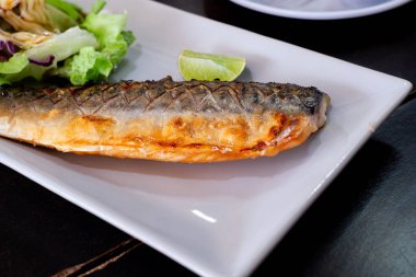 Izgara uskumru, üzerine kremalı sos ve bir dilim limon serpiştirilmiş taze yeşil salata ile beyaz tabakta servis edilir. Sağlıklı ve lezzetli bir deniz ürünleri yemeği. Yemek için mükemmel.