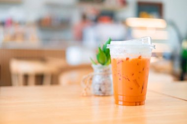 Plastik bardakta buzlu Tayland çayı. Meşhur içecek. Doğa kafesindeki ahşap masada geleneksel içecek.