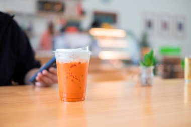 Plastik bardakta buzlu Tayland çayı. Meşhur içecek. Doğa kafesindeki ahşap masada geleneksel içecek.
