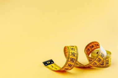 Sarı arka planda sarı şerit. Fitness için mezura ölçüyorum. Yakın plan.