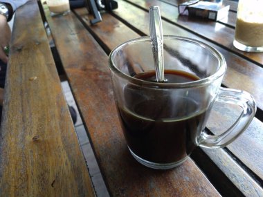 black coffee in a glass cup with a spoon