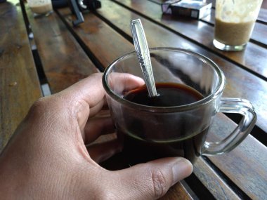 black coffee in a glass, held by hand, half full