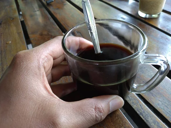 black coffee in a glass, held by hand, half full