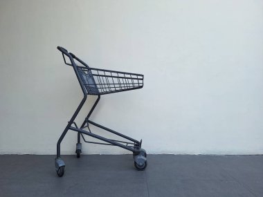 Beyaz duvar arkasında küçük gri alışveriş arabası
