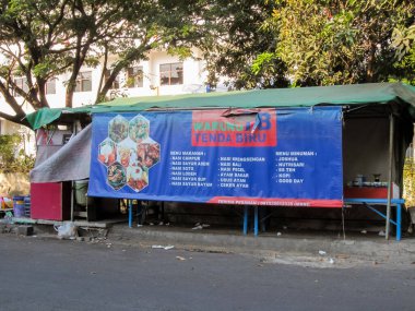 Surabaya-13 Ekim 2023: Warung Tenda Biru 'nun yol kenarında olduğunu ve çeşitli gıda ürünleri sattığını söyleyen mavi pankartlı gıda tezgahları.