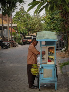 Surabaya-18 Ağustos 2023: Seyyar gıda tedarikçileri ev kompleksi etrafında yürürken mallarını satıyorlar. Çok sıkı çalışıyorlardı..