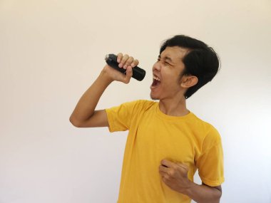 Genç yakışıklı Asyalı adamın portresi mikrofonla şarkı söylüyor. Mutlu ve rahatla, anın tadını çıkar.