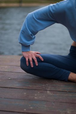 Mavi takım elbiseli atletik vücutlu bir kızın görüntüsü bulutlu yağmurlu havada yoga egzersizleri yapıyor.