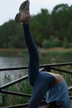 Mavi takım elbiseli atletik vücutlu bir kız bulutlu yağmurlu havalarda akrobasi egzersizleri yapıyor.