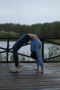 Mavi takım elbiseli atletik vücutlu bir kız bulutlu yağmurlu havalarda akrobasi egzersizleri yapıyor.