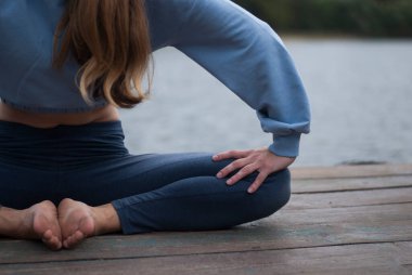 Mavi takım elbiseli atletik vücutlu bir kızın görüntüsü, Lak yakınlarında bulutlu ve yağmurlu bir havada yoga egzersizleri yapıyor.