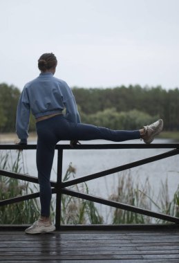 Mavi takım elbiseli atletik vücutlu bir kız bulutlu yağmurlu havalarda akrobasi egzersizleri yapıyor.