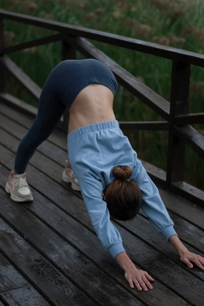 青いジムのスーツで運動体を持つ女の子のビューは パーで曇った雨の中でヨガの練習をしています — ストック写真