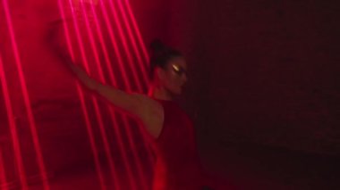 Woman in stage mini dress dances passionate Latin American tango dance in light of red laser with male partner, part of dance performance in dark with moving beams, swinging arms, turns,hugs in loft