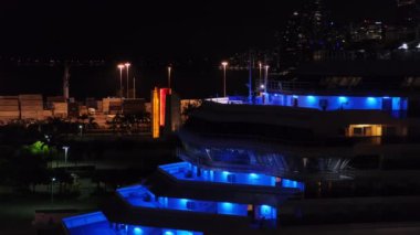 Geceleri Miami gemi terminalinde demirli olan çok katlı bir yolcu gemisine yakın çekim. Üst güverteler mavi sarı LED ışıklarla aydınlatılmış. Turist gezisi için liman, yolcu yok.