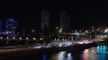 Miami, Florida 'nın kıyı kesiminin görüntüsü, Atlantik Okyanusu' ndaki renkli su yansımaları, geceleri geçen gemiden. Şehir ışıkları, aydınlık gökdelenler ve yol aydınlatması, sürüş arabaları, set otoyolu.