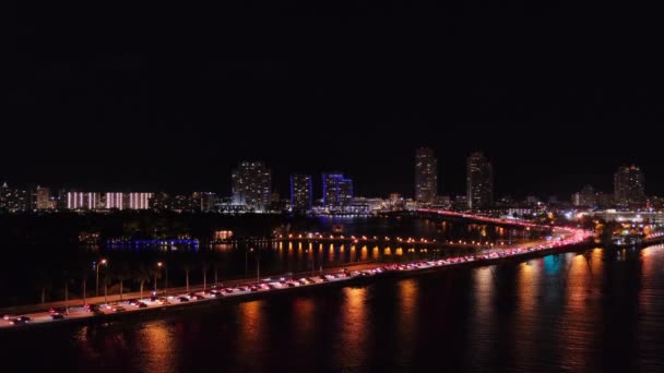 米国フロリダ州マイアミの海から遠く離れた夜のパノラマビュー 暗い水の上のマッカーサー コーズウェイ橋の蛇行道路 都市に入る交通渋滞に立っている車のライト バックグラウンドのダウンタウン — ストック動画