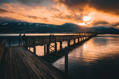 Sakin bir senfoni, turuncu gökyüzü gün yavaşça solurken sakin suları yansıtıyor. Yüksek kalite fotoğraf