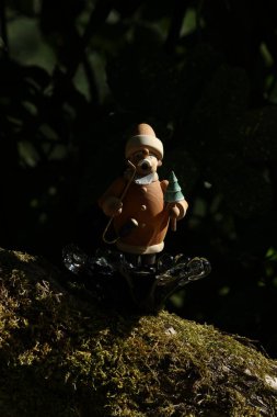 Bir ağaç kütüğünün üzerinde sırt çantasıyla duran küçük bir kurbağa figürü.