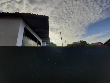 Dark wall and white house under cloudy blue sky on a sunny day