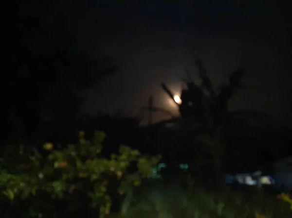 Blurred or unfocused or defocused full circle moon on empty dark sky with some banana leaves.