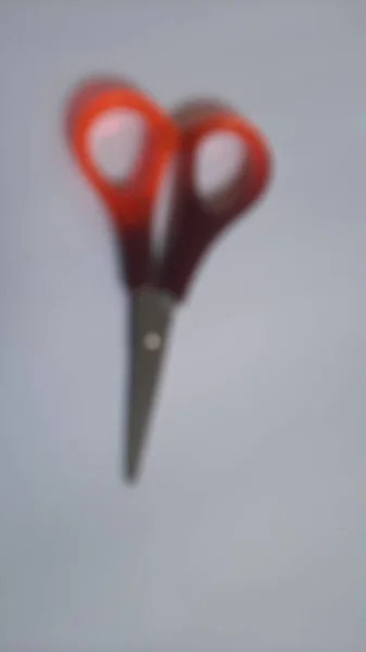 Blurred or unfocused or defocused single or one red orange brown scissors on isolated white background