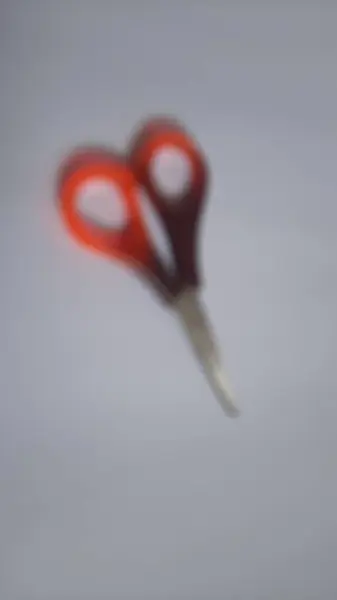 Blurred or unfocused or defocused single or one red orange brown scissors on isolated white background