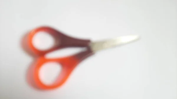 Blurred or unfocused or defocused single or one red orange brown scissors on isolated white background