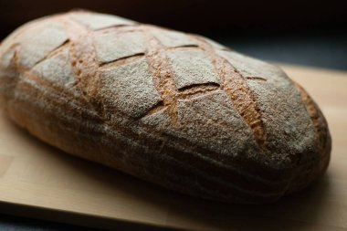 Koyu gri mutfak masasında taze pişmiş ekşi ekmek ve ahşap tahta tahta, yakın plan, açı manzaralı.