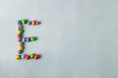 Easter candy chocolate eggs shaped in letter E, on light gray, concrete background. Preparation for holiday. Happy Easter concept. Copy space, flat lay, top view.