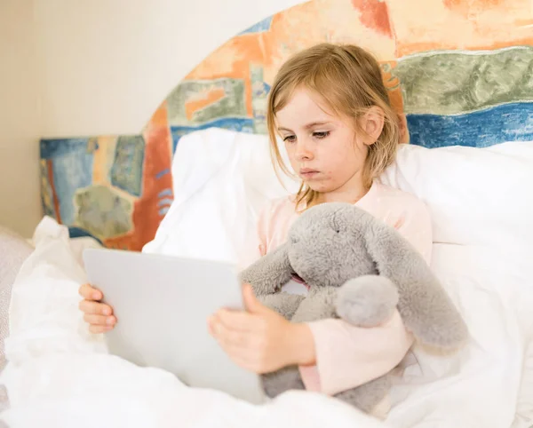 여드름을 아이가 침대에 장난감을 껴안고 있습니다 태블릿보고 바이러스 유아의 얼굴에 — 스톡 사진