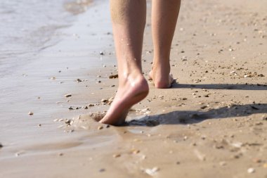 Sahilde yürüyen erkek bacaklarına yakın çekim. Çıplak ayakla ıslak kumda yürüyorum. Tatil konsepti, tanınmayan kişi