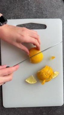 Limonu beyaz dilimlere kesen kadının elleri gri beton masa, üst manzara.