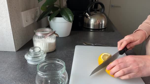 白い切断板にレモンを切った女性の手 ケトル ガラス瓶砂糖 プラント コンクリートキッチンカウンター — ストック動画