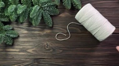 Kadınların elleri kıvrılmış pamuk halat, jüt ip ve makasları ladin dallarıyla süslenmiş siyah ahşap masaya koyar. El yapımı el işi kavramı, Noel ve kış tatili